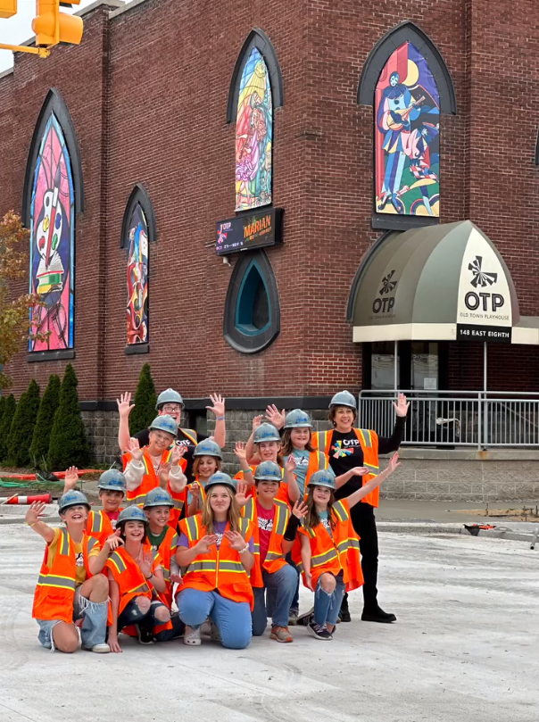 Young Company Members wearing orange vests and hard hats celebrate the opening of the Eighth and Cass Street intersection.